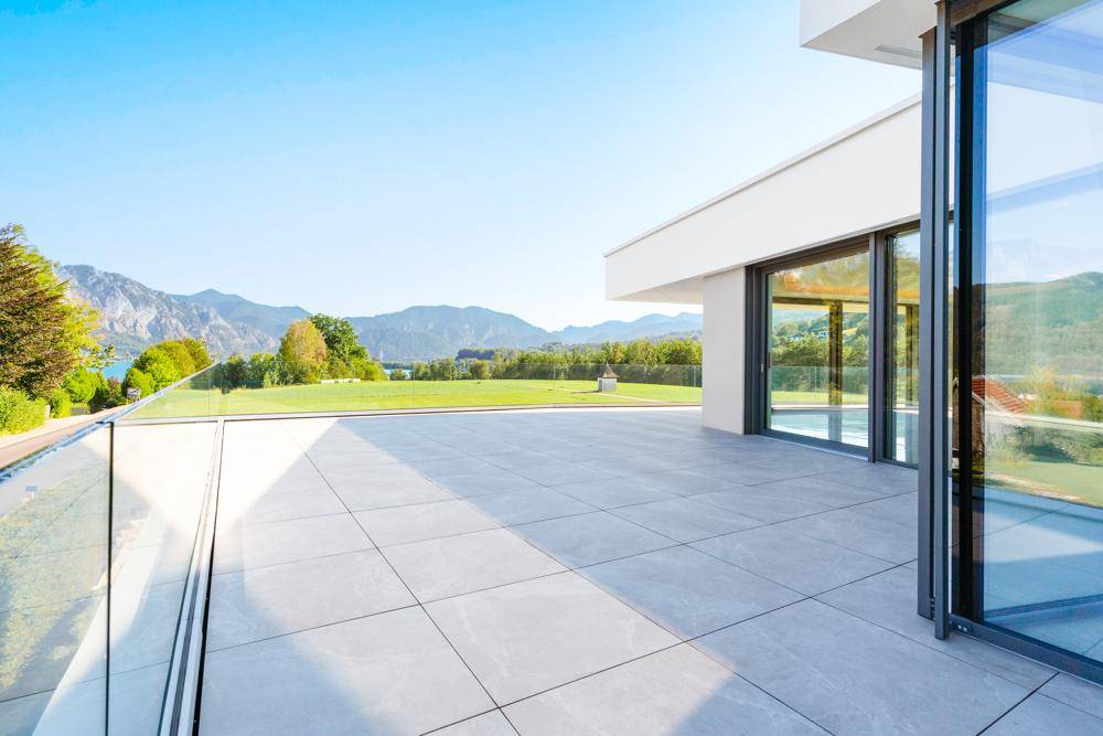 Geräumige Terrasse mit Fliesenboden und weitem Blick auf grüne Felder und die majestätischen Berge.