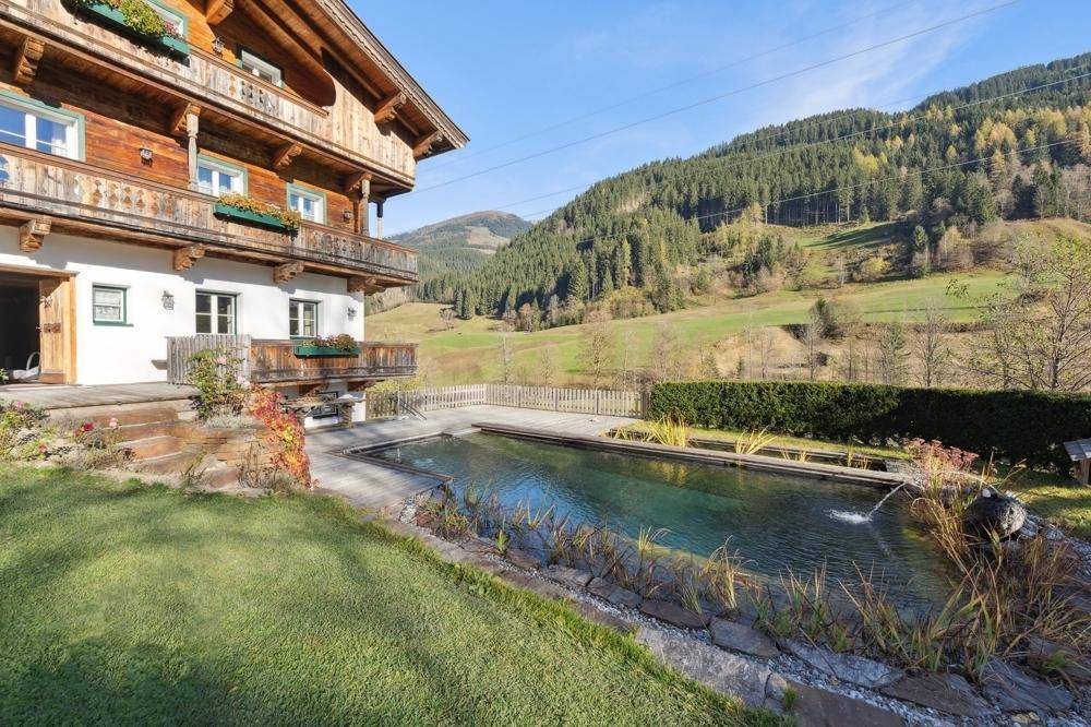 Nahaufnahme des traditionellen Holzhauses mit Naturpool und weitem Blick auf die umliegende Berglandschaft.