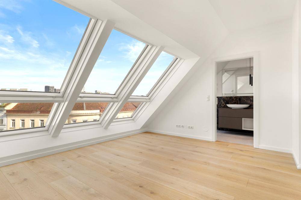 Helles Schlafzimmer im Dachgeschoss mit Holzboden und direktem Zugang zum modernen Badezimmer.