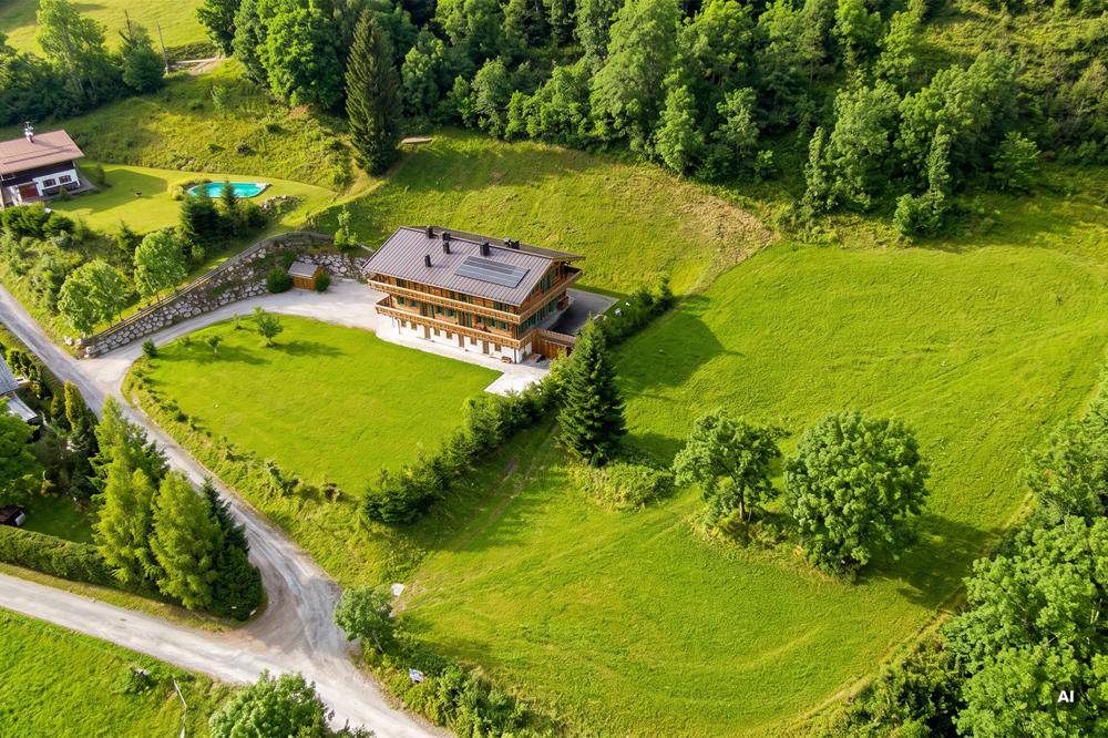 Luftaufnahme eines Anwesens mit modernem Haus, weitläufigen Grünflächen, Bäumen und einem kleinen Poolbereich.