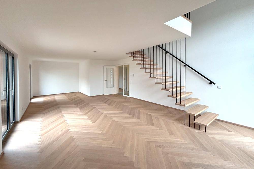 Heller Wohnbereich mit modernem Fischgrätparkett und offener Treppe zum Obergeschoss.