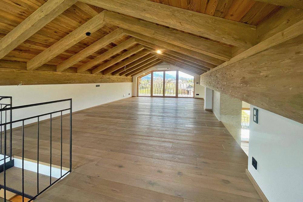Geräumiger Dachboden mit sichtbaren Holzbalken, Holzboden und Zugang zu einem Balkon mit Aussicht.