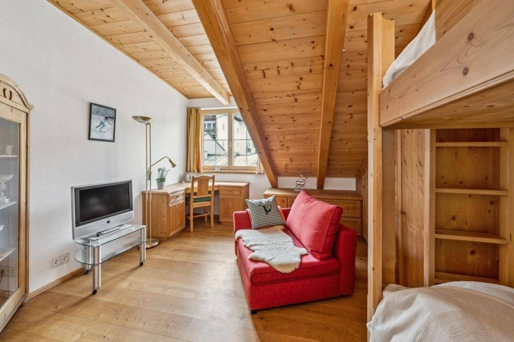 Gemütliches Schlafzimmer mit Etagenbett, Schreibtisch und Holzelementen unter dem Dach.