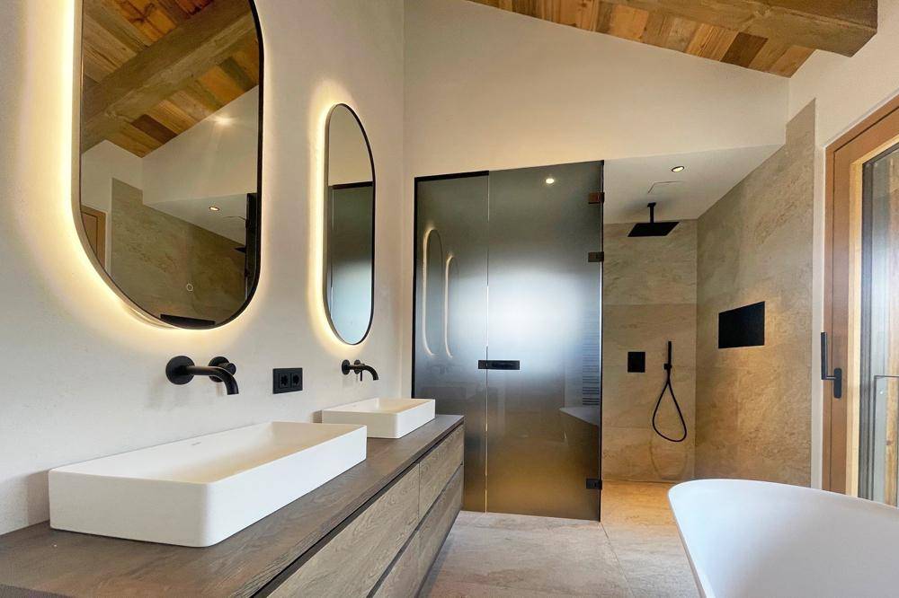 Luxuriöses Badezimmer mit Doppelwaschbecken, beleuchteten Spiegeln, freistehender Badewanne und Glasdusche.