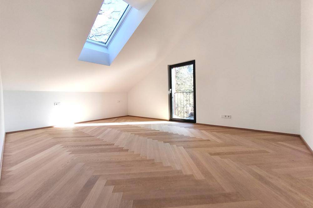 Helles Zimmer im Dachgeschoss mit Fischgrätparkett, Dachfenster und Zugang zu einem französischen Balkon.