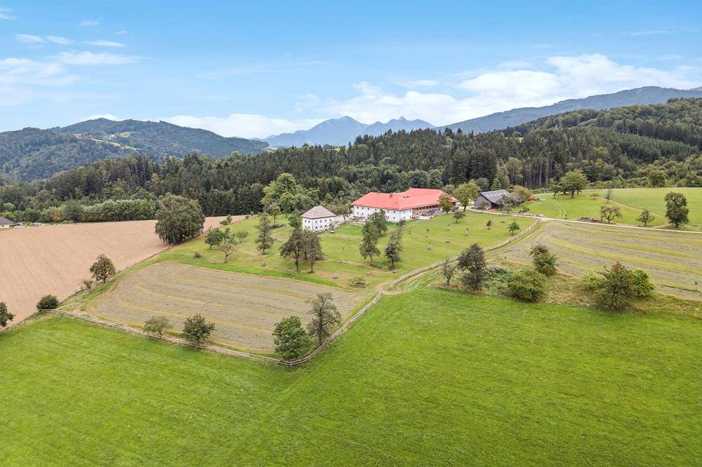 Weitläufige Luftaufnahme des Anwesens, eingebettet in eine malerische Landschaft mit Feldern und bewaldeten Hügeln.
