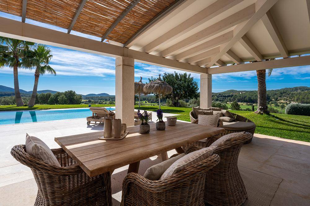 Gemütliche überdachte Terrasse mit Esstisch und Korbmöbeln, direkt am Pool gelegen.