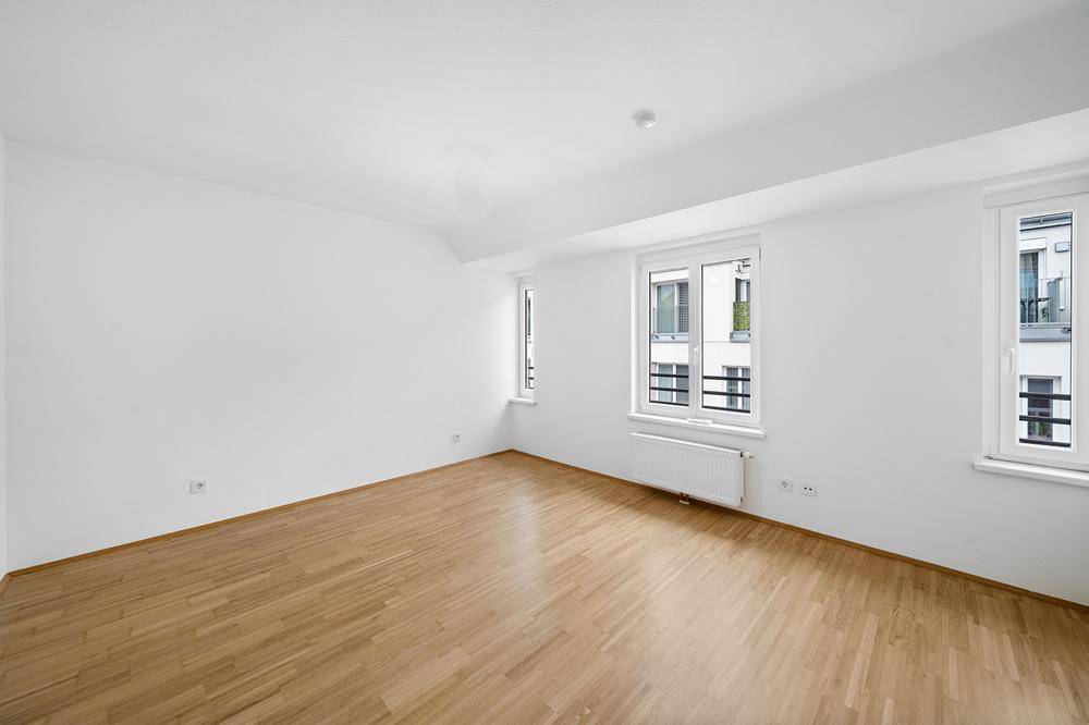 Geräumiges, helles Zimmer mit Holzboden und mehreren Fenstern, ideal für Wohn- oder Schlafbereich.