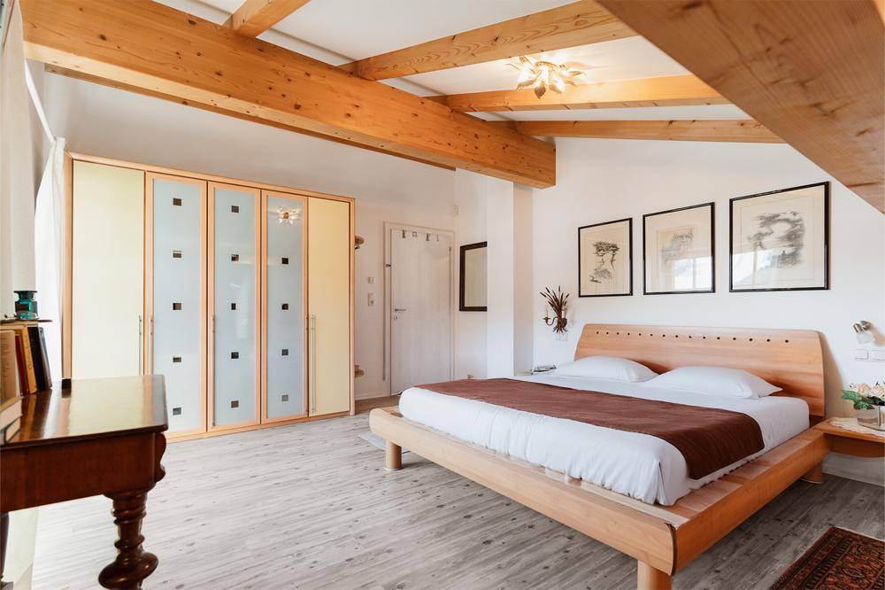 Gemütliches Schlafzimmer mit sichtbaren Holzbalken, Holzboden und einem großen, modernen Kleiderschrank.