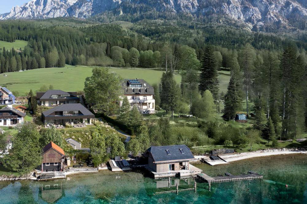 Luftaufnahme einer exklusiven Wohnanlage am Seeufer mit Bootsanlegestellen und Bergpanorama.