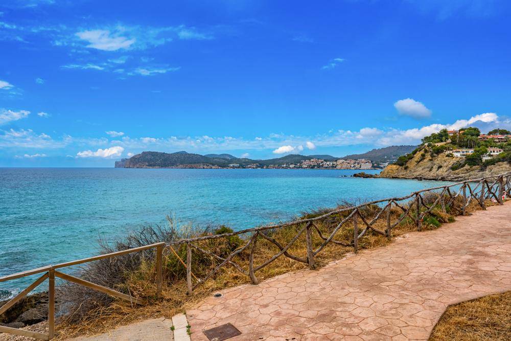 Küstenweg mit rustikalem Holzzaun und weitem Blick über das Meer und eine malerische Küstenstadt.