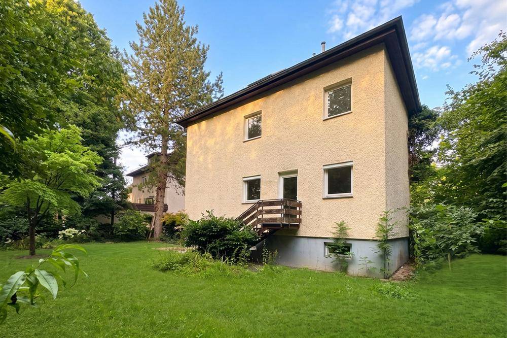 Rückansicht des gelben Hauses mit Holztreppe und weitläufigem Garten.