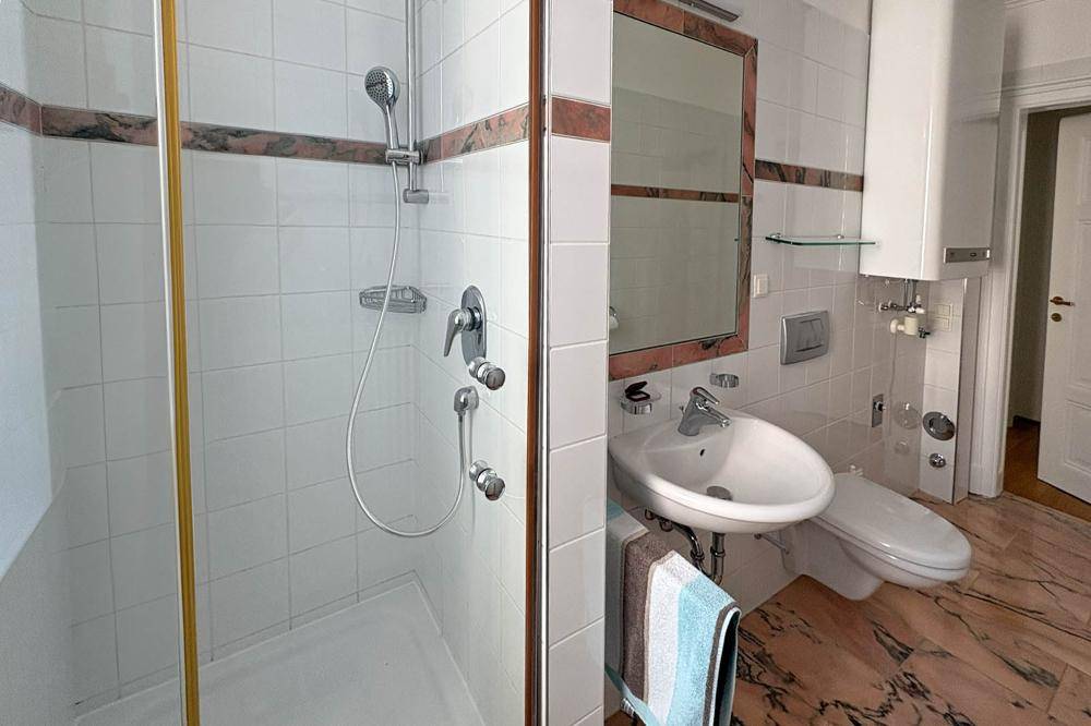 Badezimmer mit Dusche, Waschbecken und WC, ausgestattet mit weißen Fliesen und Marmorboden.