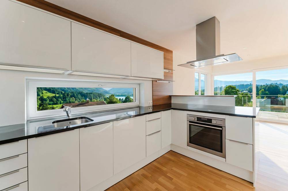 Moderne Einbauküche mit weißen Hochglanzfronten, schwarzer Arbeitsplatte und Seeblick.