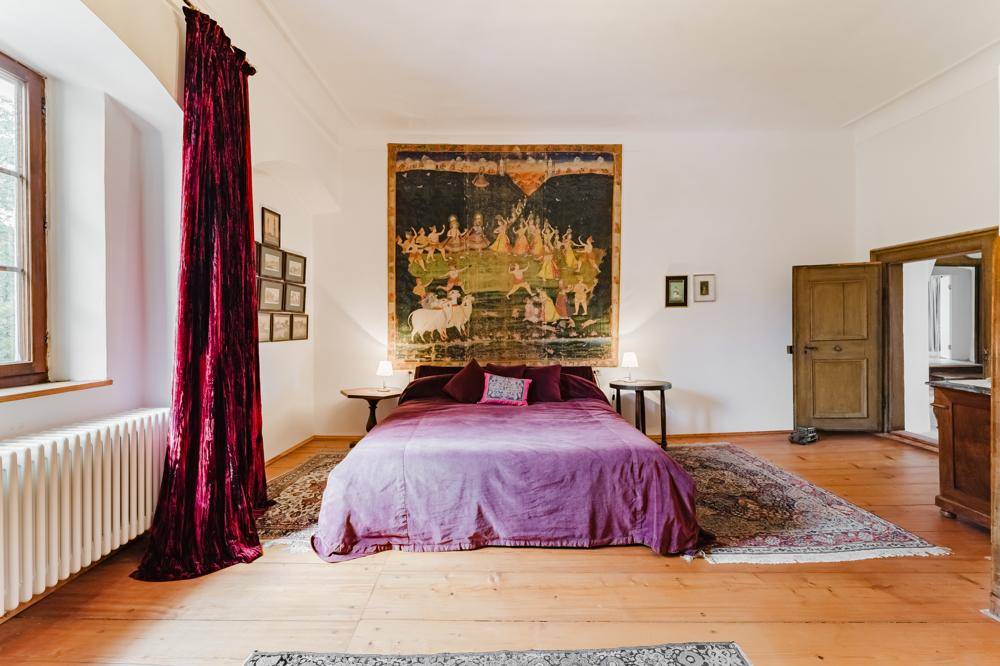 Gemütliches Schlafzimmer mit lila Bett, Holzdielenboden, traditionellen Teppichen und einem großen Wandteppich.