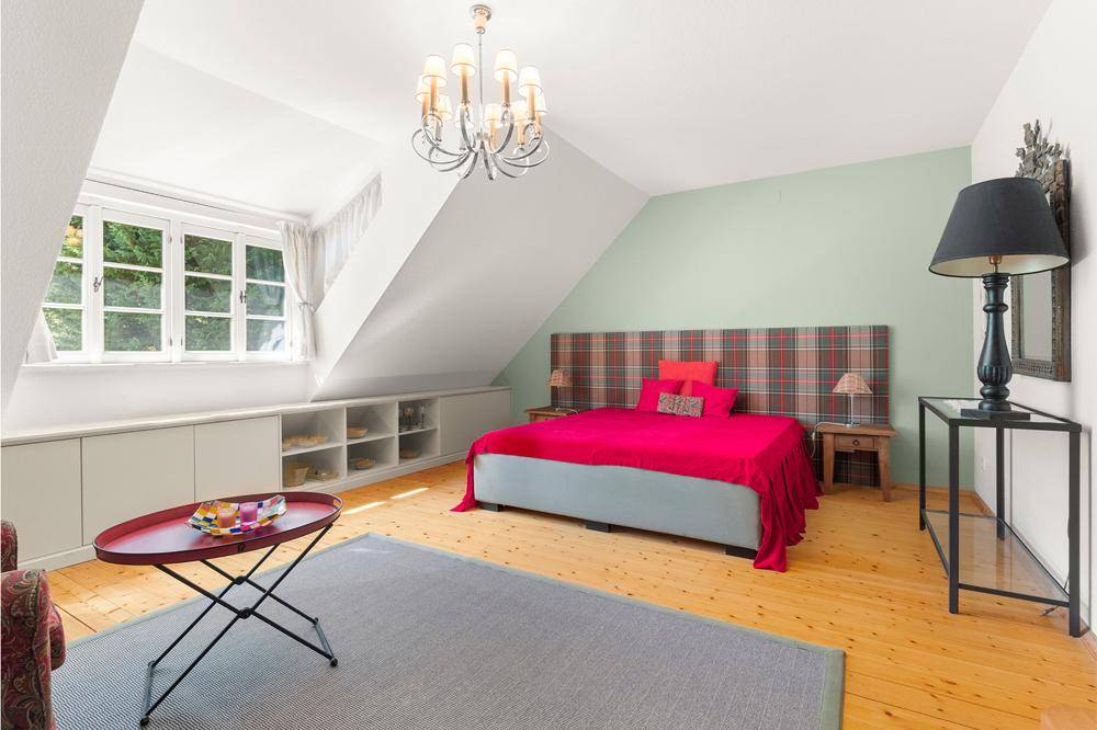 Gemütliches Schlafzimmer im Dachgeschoss mit Holzdielenboden, Dachschrägen und großen Fenstern.