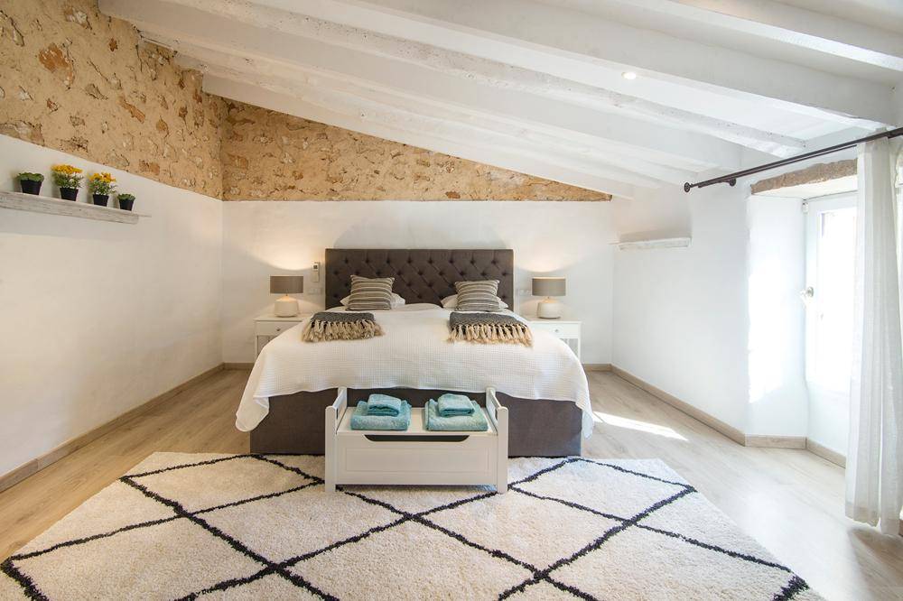 Geräumiges Schlafzimmer mit Dachschräge, freigelegter Steinwand und Holzbalkendecke.