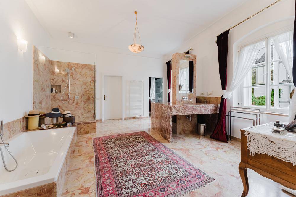 Großes Luxusbadezimmer mit Marmorböden und -wänden, Badewanne, begehbarer Dusche und Doppelwaschbecken.