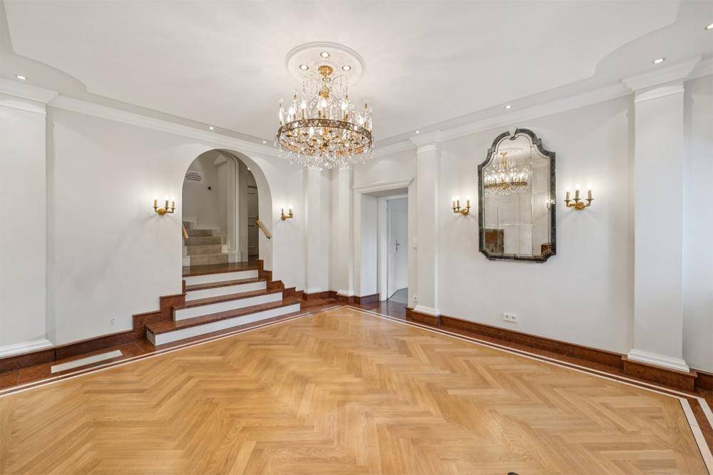 Eleganter Eingangsbereich mit Fischgrätparkett, Kronleuchter und einem dekorativen Wandspiegel.