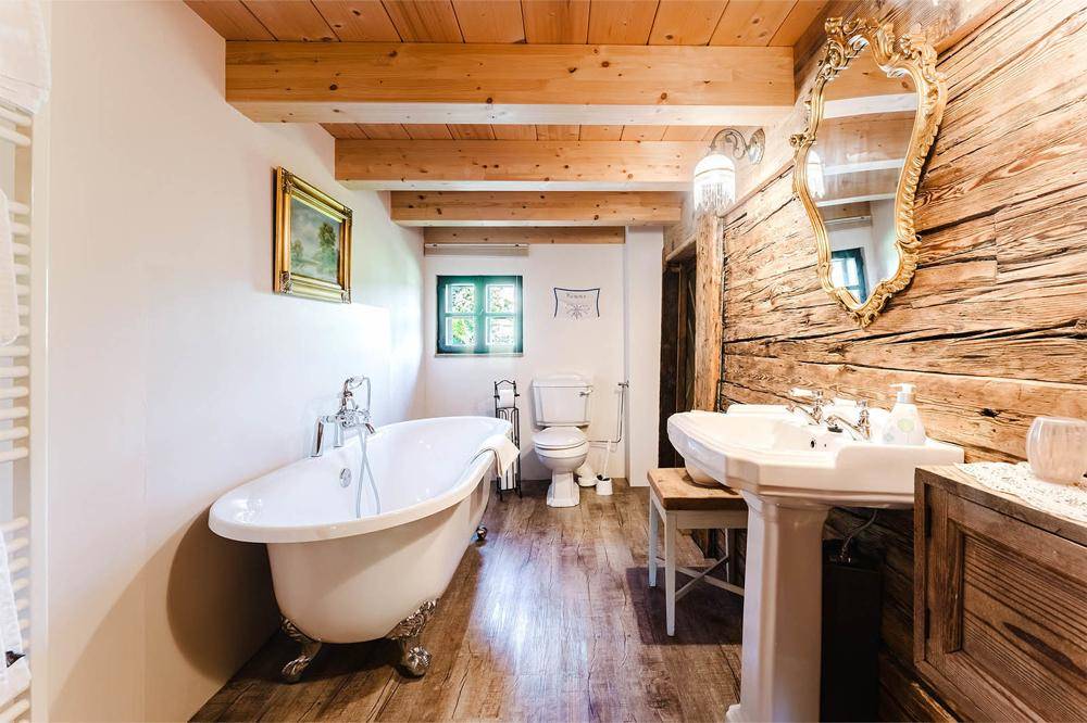 Rustikales Badezimmer mit freistehender Badewanne, Holzwand und Holzbalkendecke.