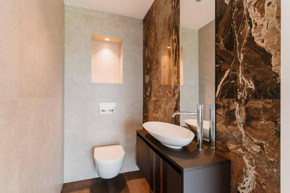 Modernes Gäste-WC mit elegantem Waschbecken, Wand-WC und luxuriöser Marmorwand.
