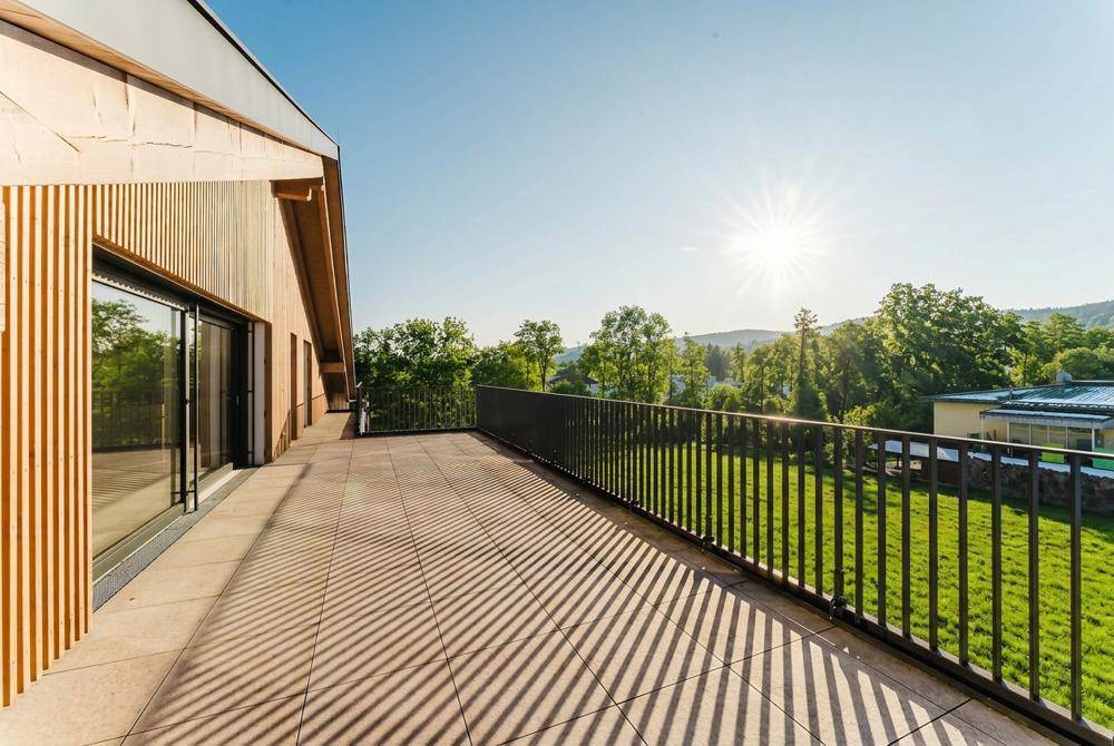 Große, sonnige Terrasse mit Blick ins Grüne und moderner Holzfassade des Gebäudes.