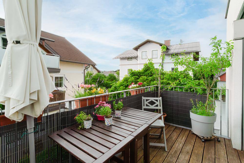 Sonniger Balkon mit Holzboden, Esstisch und Blumenkästen, ideal für Mahlzeiten im Freien.