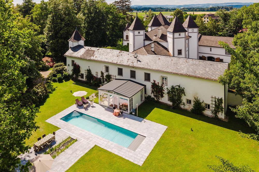 Weitläufiger Gartenbereich mit großem Swimmingpool und einem eleganten Wintergarten am historischen Gebäude.
