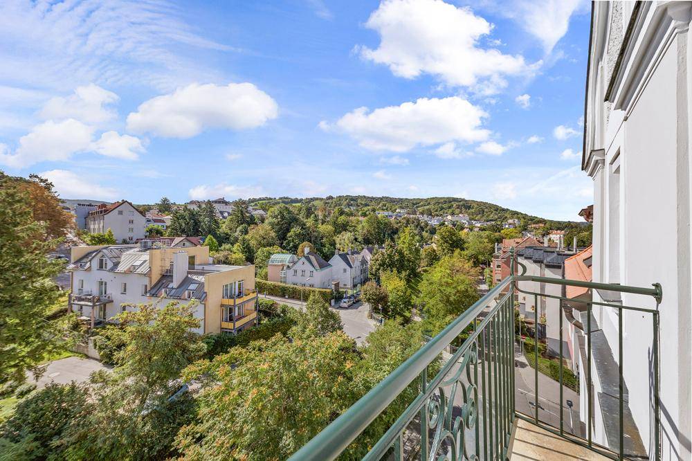 Panoramablick vom Balkon über eine grüne Wohngegend mit bewaldeten Hügeln unter blauem Himmel.