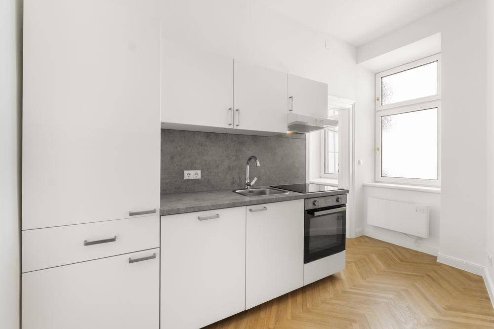 Moderne, helle Küchenzeile mit weißen Fronten und integrierten Geräten, ideal für kleine Wohnungen.