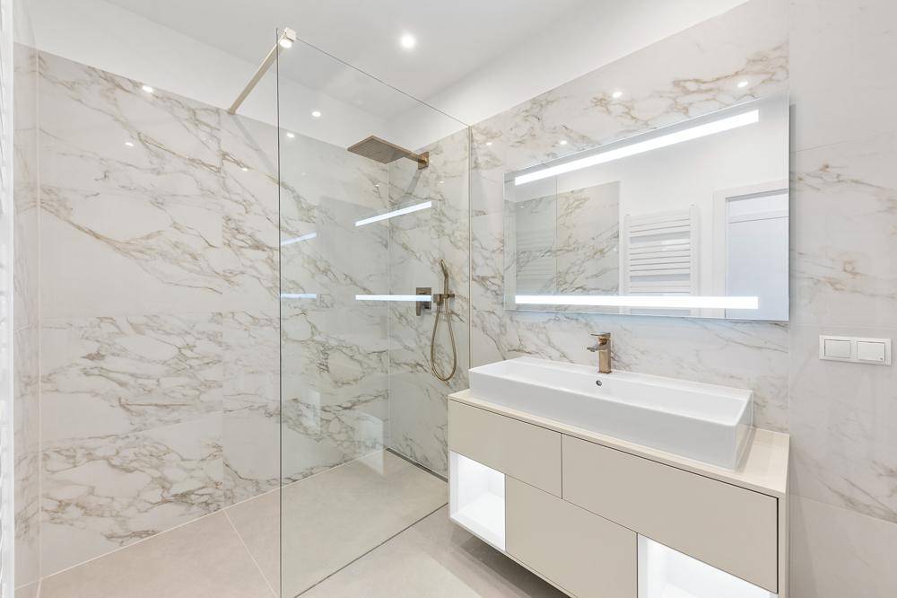 Elegantes Badezimmer mit Marmorfliesen, großer begehbarer Dusche und modernem Waschtisch.