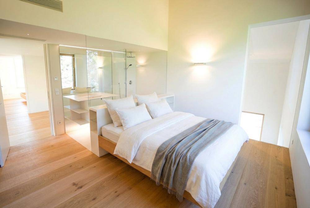 Helles Schlafzimmer mit Holzboden und offenem, modernem Badezimmerbereich, der viel natürliches Licht hereinlässt.