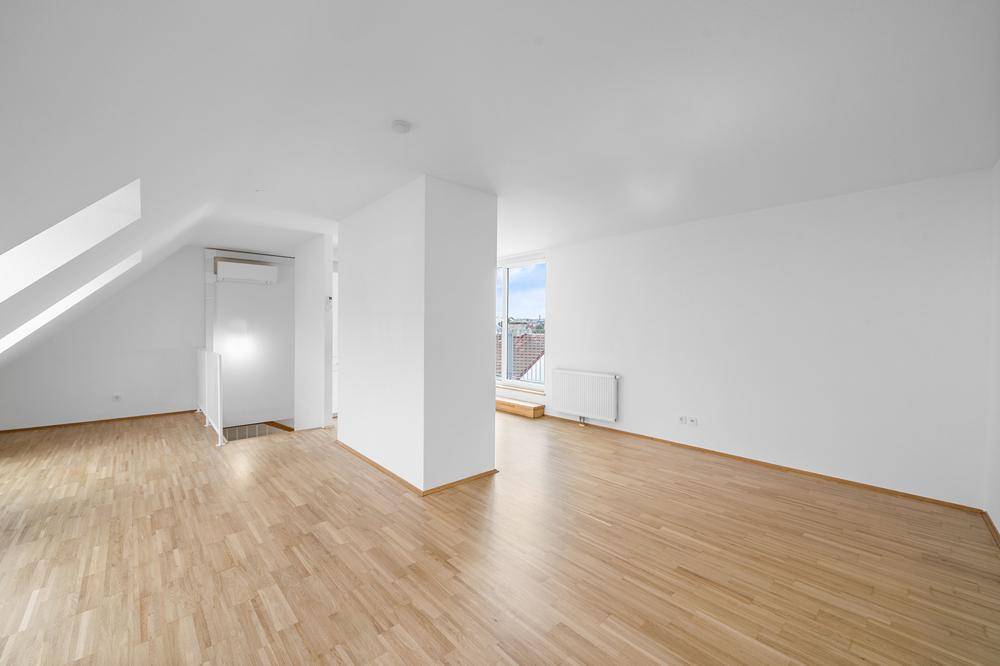 Helles Zimmer im Dachgeschoss mit Holzboden und schrägen Wänden, bereit zur individuellen Gestaltung.