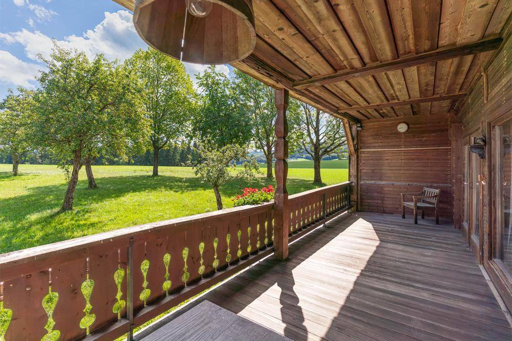 Großer Holzbalkon mit traditionellem Geländer und weitem Blick auf die grüne Landschaft.