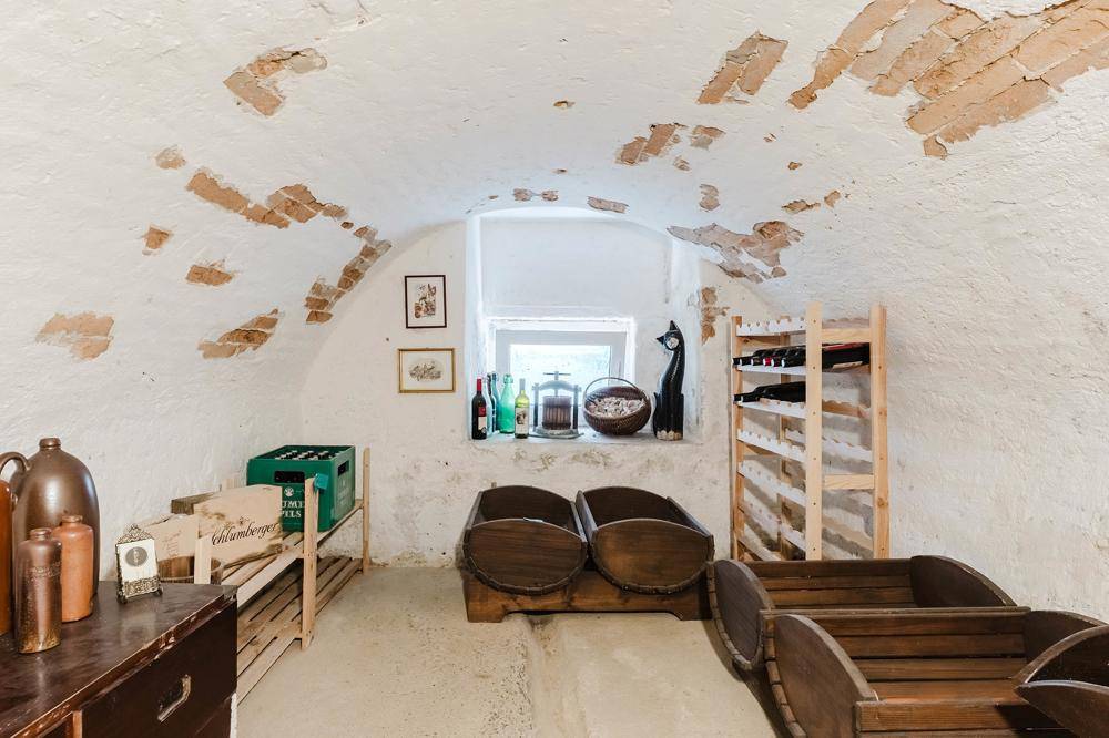 Rustikaler Weinkeller mit Gewölbedecke, unverputzten Ziegeln und Holzregalen für Flaschen.