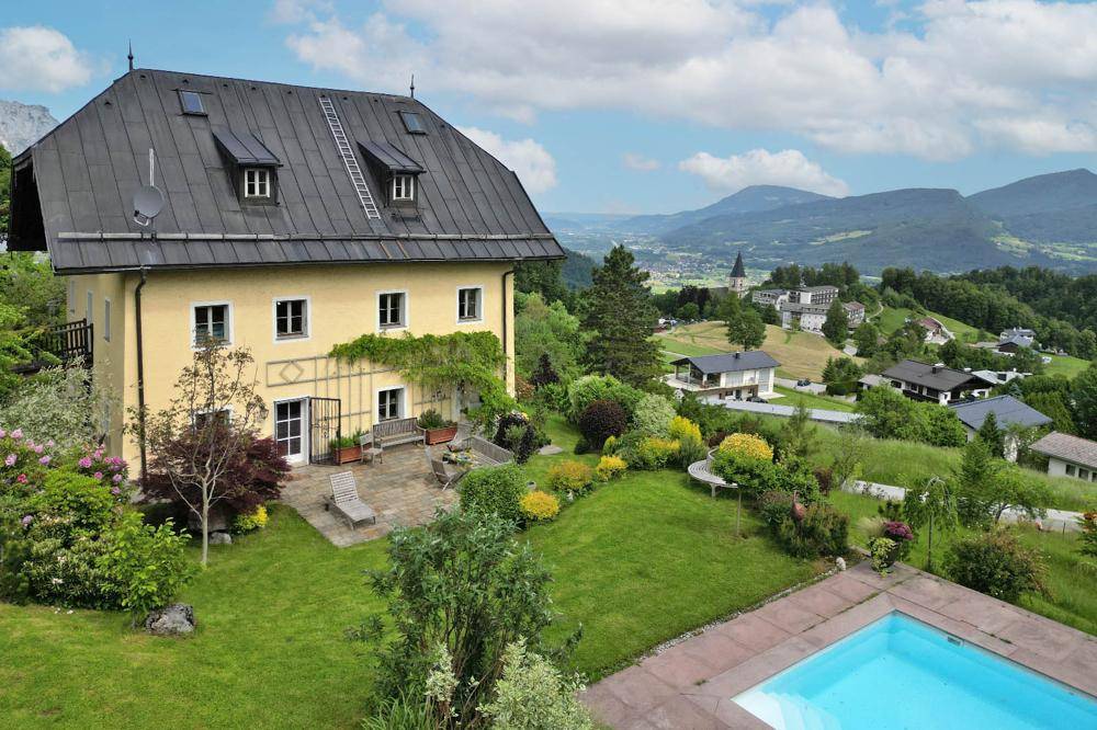 Hausfassade mit Terrasse, Garten und Pool, bietet einen weiten Blick über das Tal und die Berge.