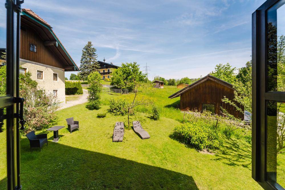 Grüner Garten mit Liegestühlen und Sitzgelegenheiten, umgeben von ländlicher Natur.