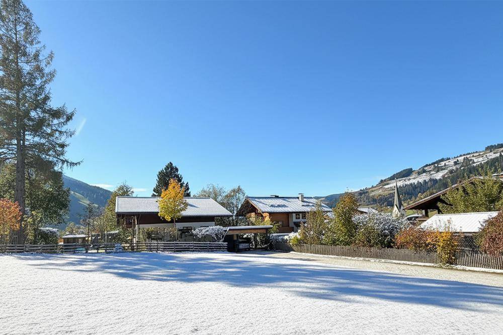 Weitläufige Winterlandschaft mit verschneiten Feldern, Häusern und bewaldeten Bergen im Hintergrund.