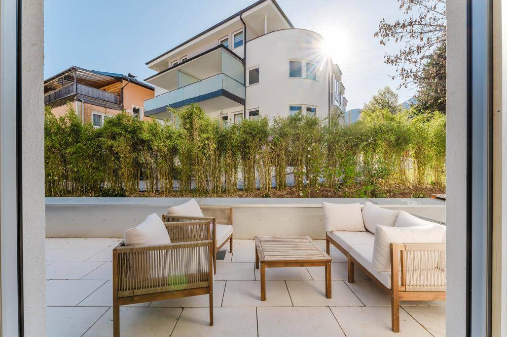 Sonniger Außenbereich mit moderner Terrasse, Sitzgelegenheiten und Bambusbepflanzung.