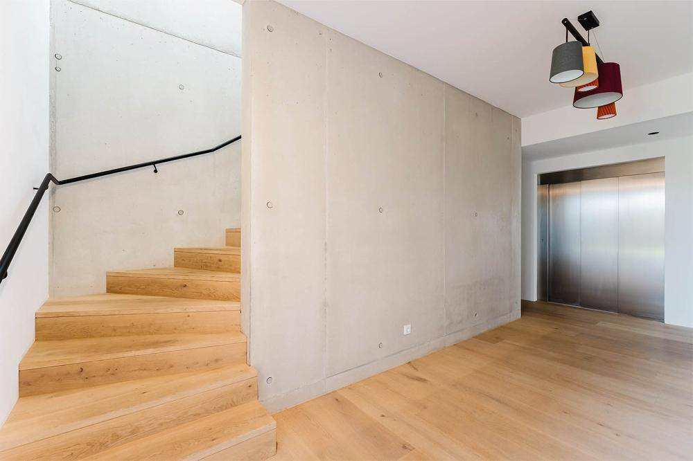 Moderner Eingangsbereich mit Holztreppe, Sichtbetonwand und Aufzug.