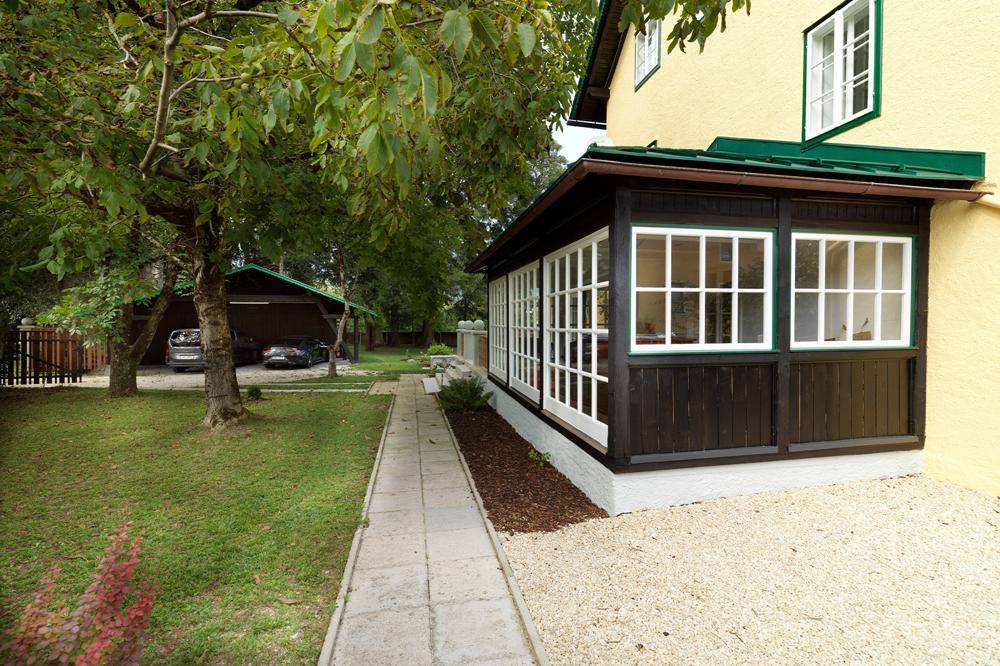 Seitlicher Anbau mit verglastem Wintergarten und einem gepflasterten Weg im Grünen.