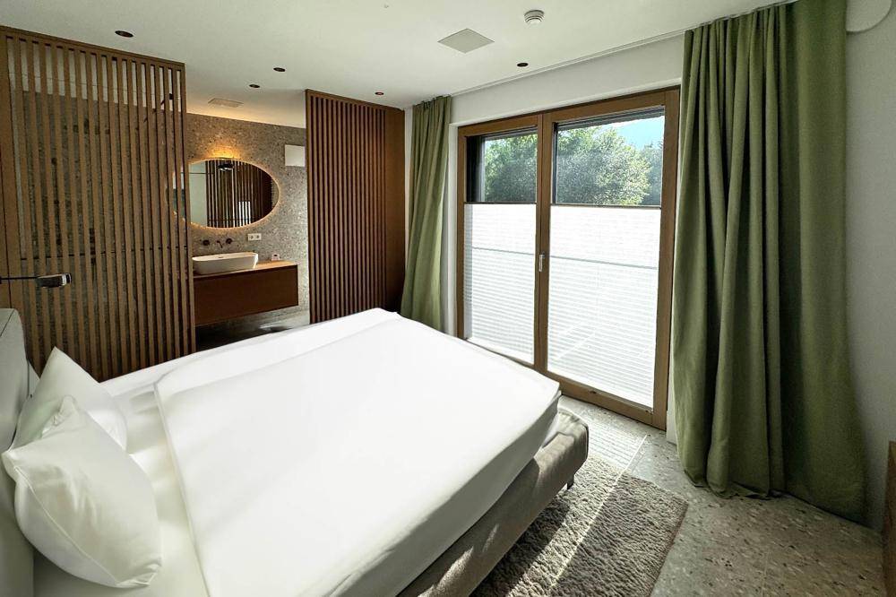 Gemütliches Schlafzimmer mit Holzelementen, großem Fenster und angrenzendem Waschbereich.