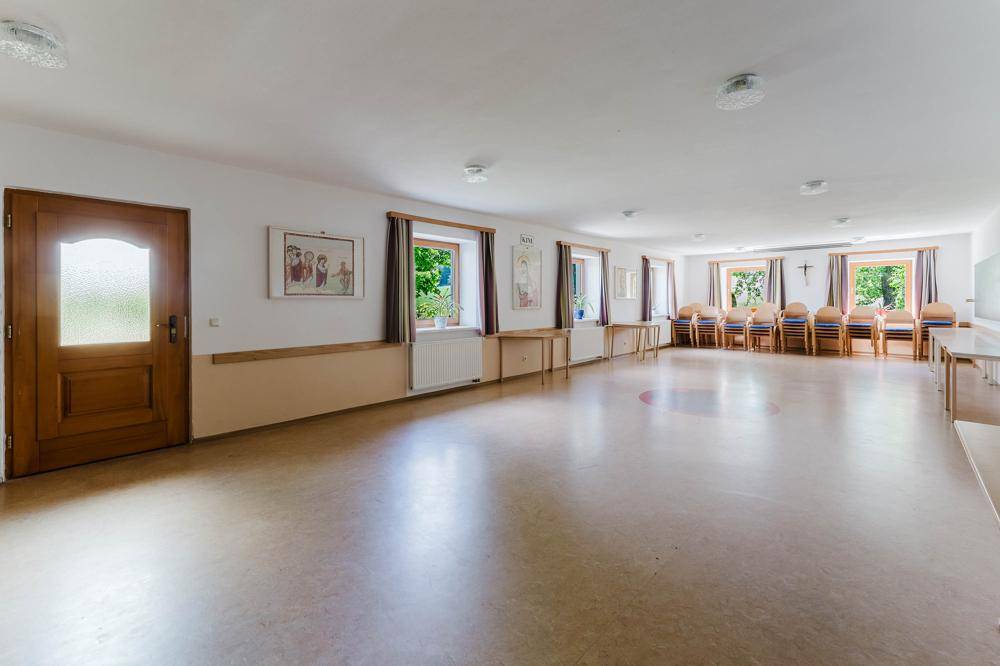Großer, heller Mehrzweckraum mit mehreren Fenstern und einer Holztür, ideal für Veranstaltungen.