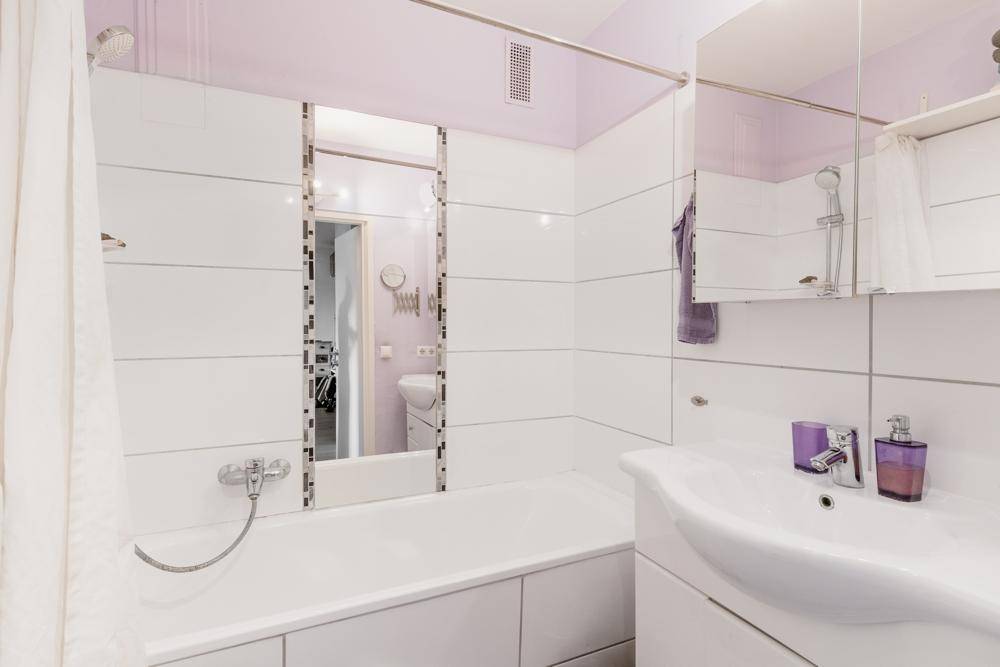 Helles Badezimmer mit Badewanne, Dusche, weiß gefliesten Wänden und einem einzelnen Waschbecken.