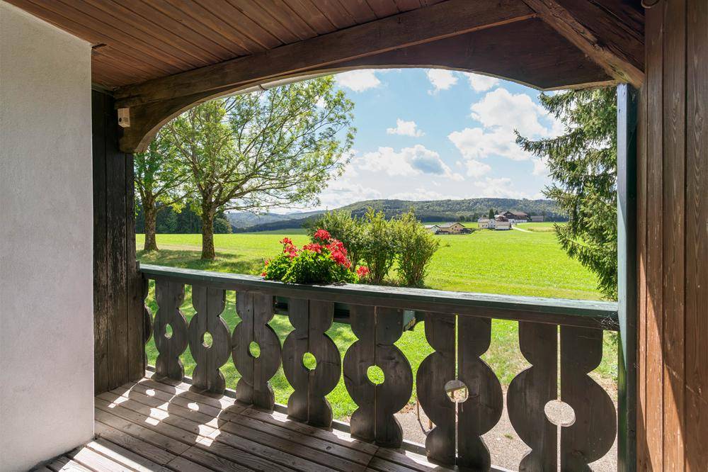 Überdachter Holzbalkon mit geschnitztem Geländer und idyllischem Ausblick auf die hügelige Landschaft.