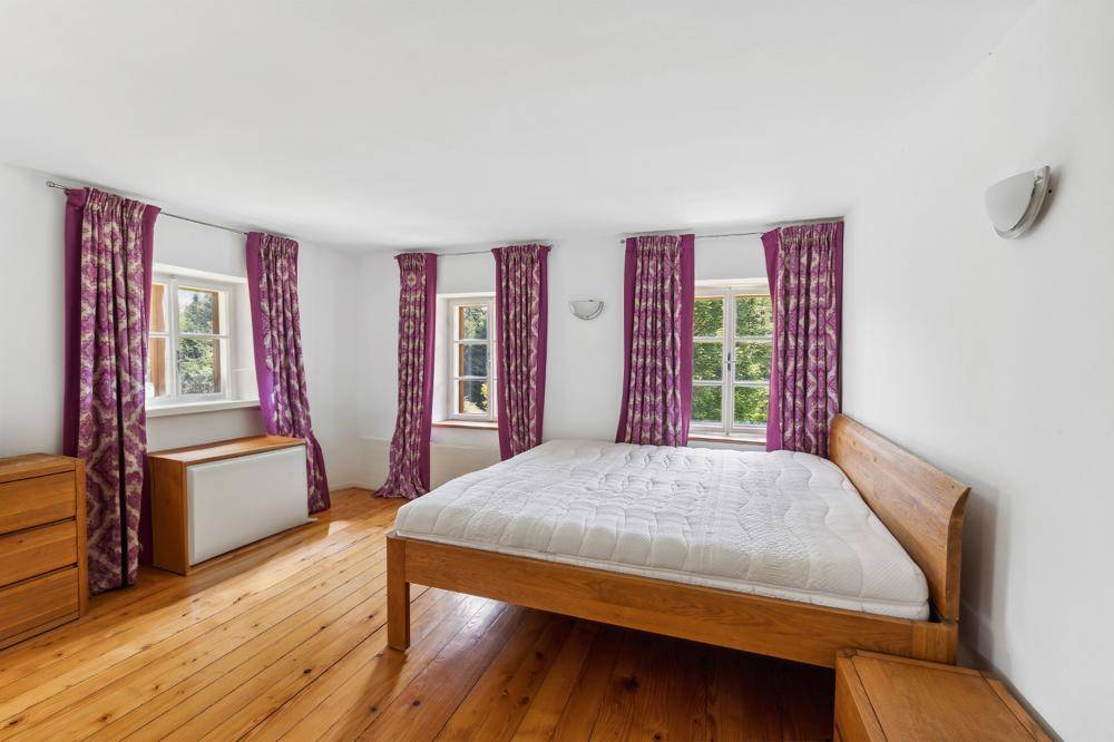 Helles Schlafzimmer mit Holzboden, weißen Wänden und auffälligen lila Vorhängen, bietet eine gemütliche Atmosphäre.