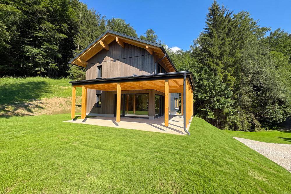 Rückseite des modernen Hauses mit großer überdachter Holzterrasse und weitläufigem Rasen.