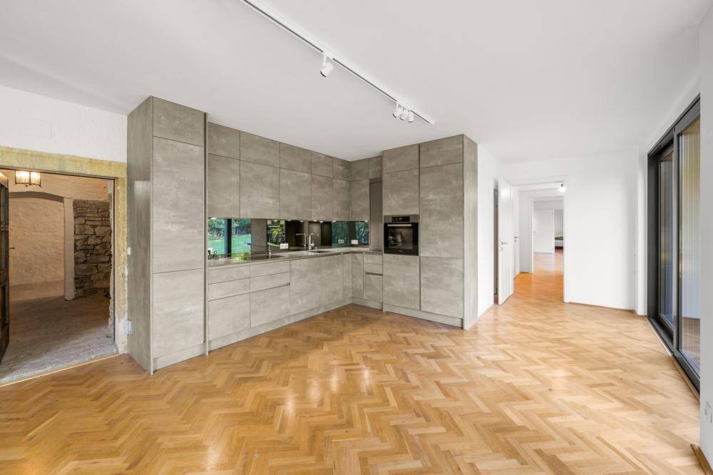 Moderne Küche mit grauen Schränken und Fischgrätparkett, offen zu angrenzenden Wohnbereichen.