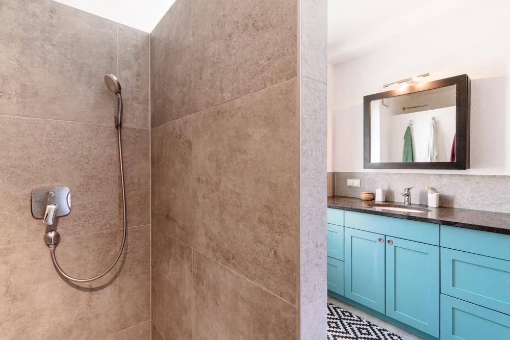 Modernes Badezimmer mit begehbarer Dusche, türkisfarbenem Waschtisch und großformatigen Fliesen.