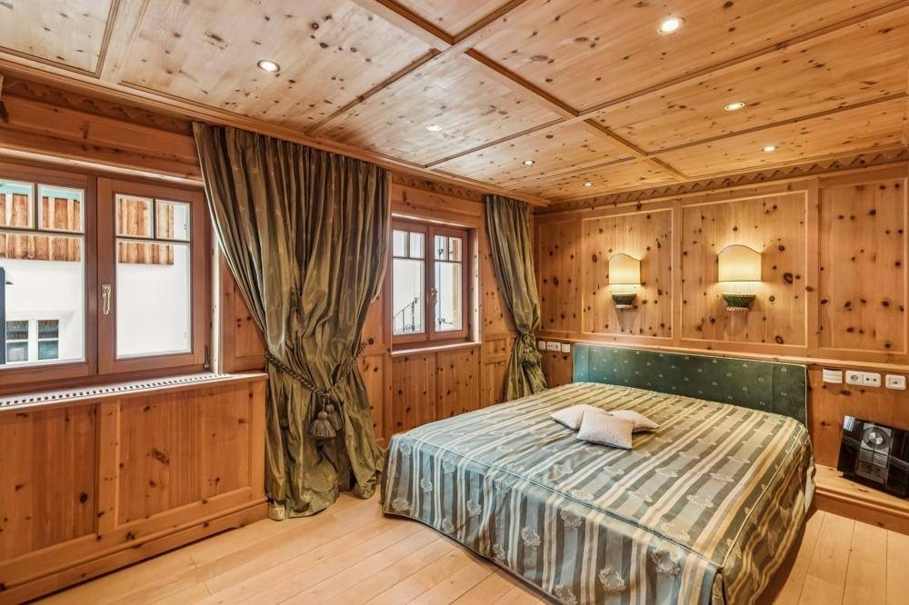 Komfortables Schlafzimmer mit Holzvertäfelung, Doppelbett und grünen Vorhängen in traditionellem Ambiente.